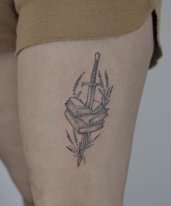 Sword going through books tattoo on the thigh