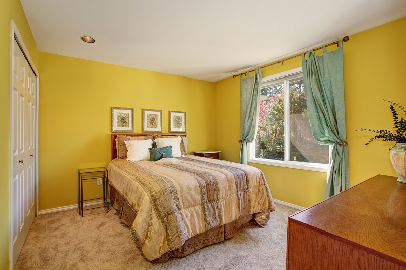 Bright,bedroom,with,yellow,interior,paint,and,beautiful,decorative,bedding.