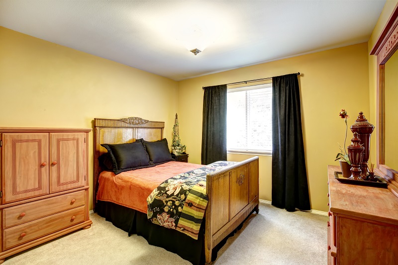 Bright,yellow,bedroom,with,rustic,carved,wood,bed,,dresser,and